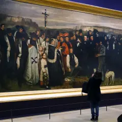 Obraz przedstawia pogrzeb w Ornans, z żałobnikami i duchownymi zgromadzonymi wokół krzyża.