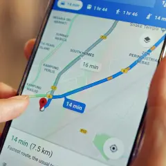 Palec wskazuje na mapę na ekranie telefonu, pokazując trasę z szacowanym czasem 14 minut. Możesz łatwo wysłać pinezkę z lokalizacją.