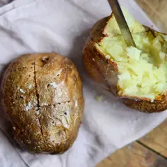 Två gyllene bakade potatisar i airfryer, en med en kniv som skär i det fluffiga inre. Perfekt för en snabb och god måltid.