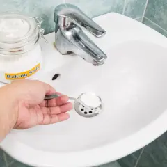 Une main verse du bicarbonate de soude dans un évier, une méthode naturelle pour le déboucheur canalisation maison.