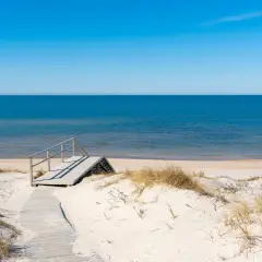 Drewniane schody prowadzą na piaszczystą stegna plaża. Błękitne morze i niebo tworzą spokojny krajobraz.