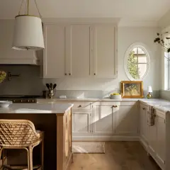 A bright, airy Studio McGee kitchen with cream cabinetry, a large island, woven stools, and a charming oval window.