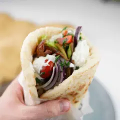 En hand håller en gyros med kött, grönsaker och sås. Perfekt för en supergod fredagsmat!