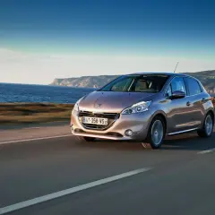 En Peugeot 208 kör längs en kustväg med havet till vänster och berg i bakgrunden. En perfekt bild för ett peugeot 208 test.