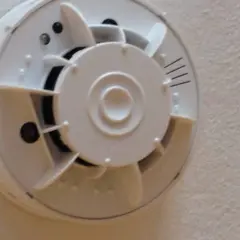 Ein weißer Rauchmelder mit integrierter Kamera, der an einer Decke montiert ist.