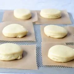 Seis bolas de fraile crudas, listas para hornear, descansan sobre papel de horno en una bandeja metálica.