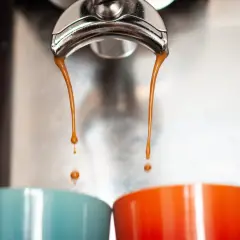 Gorące, aromatyczne espresso co to? Dwie strumienie kawy spływają do kolorowych filiżanek.