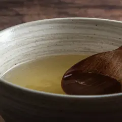 A wooden spoon rests in a bowl of clear, golden broth, hinting at the subtle flavors of various types of dashi.