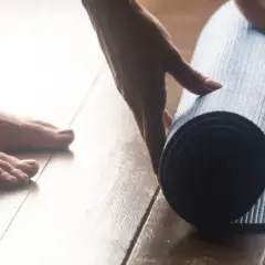 Pieds nus sur un parquet, une main déroule un tapis bleu pour une séance de sport à la maison.