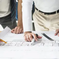 Manos trabajando en planos, con lápiz y marcador, revisando la escritura de división horizontal.