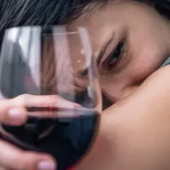 Smutna kobieta z kieliszkiem wina, symbolizująca 6 objawów uzależnienia od alkoholu.