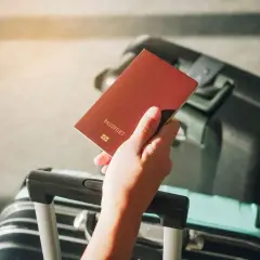 Dłoń trzyma paszport, obok walizka. Problem z wyrabianiem nowego dokumentu z powodu braku starego paszportu.