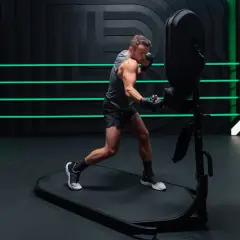An orthodox fighter trains intensely, throwing punches at a boxing dummy in a modern gym with neon green accents.