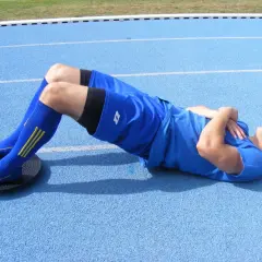 Mężczyzna wykonuje ćwiczenia na równowagę na bieżni, leżąc na plecach z nogami na platformie balansującej.