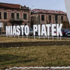 Napis "Miasto Piątek" na tle starych kamienic. To środek Polski, gdzie każdy dzień może być jak piątek.