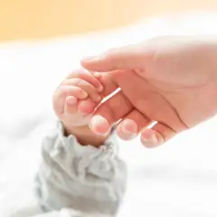 Delikatny chwyt pęsetkowy małego paluszka niemowlęcia przez dorosłą dłoń.