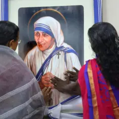 Frauen berühren ein Bild von Mutter Teresa, die ihr Leben den Armen widmete.