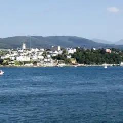 Vista del mirador de Ribadeo con casas blancas y el mar azul. Un pequeño barco navega en la distancia.