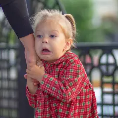 Małe dziecko z przerażoną miną mocno trzyma się ręki dorosłego. To typowy lęk separacyjny u 2-latka, gdy czuje się niepewnie.