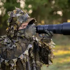 Fotograf w maskującym stroju z liśćmi używa aparatu do fotografowania zwierząt, by uchwycić dziką przyrodę.