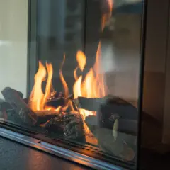 Flammen tanzen um Holzscheite in einem modernen Kamin. Ein Blick, der zeigt, wie man Ascheflecken entfernen kann, ohne die Gemütlichkeit zu stören.