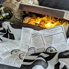 Un coffre au trésor ouvert, rempli de pièces d'or, est entouré de cartes de jeu sur le thème des pirates. Ces cartes expliquent c'est quoi un dialogue, avec des contextes et des objectifs pour écrire des scènes.