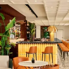 Interni eleganti del Bulgari Hotel Roma: bancone bar dorato, sedie in pelle arancione, piante lussureggianti e un'atmosfera sofisticata.