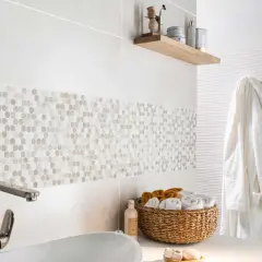 Détail d'une salle de bain moderne avec une bande de pose de faïence en mosaïque hexagonale. Un panier de serviettes et un peignoir blanc complètent la scène.