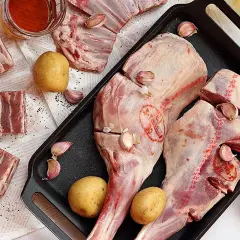 Pierna de cordero cruda con patatas, ajos y aceite de oliva, lista para asar.