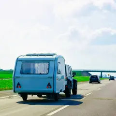 Samochód terenowy ciągnie dmc przyczepy kempingowej po autostradzie. W tle zielone pola i most.