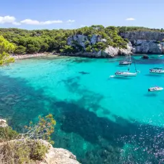Calas turquesas y veleros, ideal para saber qué ver en Menorca en 3 días. Disfruta de playas paradisíacas y acantilados verdes.