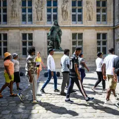 Un groupe de jeunes explore les musées de Paris, admirant une statue devant un bâtiment historique.