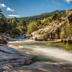 Río serpenteante entre rocas y vegetación, con una montaña boscosa al fondo, un paisaje idílico cerca de Madrid.