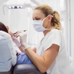 Dentista con mascherina esamina i denti di un paziente. La pulizia dei denti dura circa 30-60 minuti.