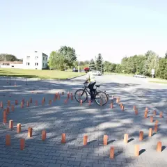 Osoba na rowerze w kamizelce odblaskowej i kasku manewruje między słupkami. To część testów na kartę rowerową.