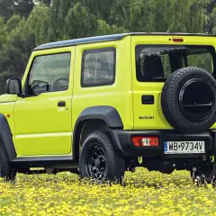 Jaskrawożółty Suzuki Jimny na tle łąki z żółtymi kwiatami. Sprawdź aktualną suzuki jimny cena i możliwości tego terenowego auta.