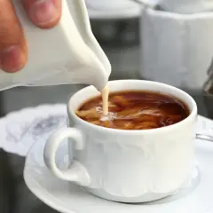 Eine Hand gießt Milch in eine Tasse Kaffee. Der cremige Kaffe milch Strudel tanzt im heißen Getränk.