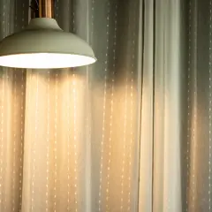 Jasna lampa wisząca rzuca ciepłe światło na zasłony. Czy 3000 lumenów to dużo? To dużo światła do stworzenia przytulnej atmosfery.