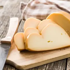Tagli di **la provola** affumicata su un tagliere di legno, accanto a un coltello.