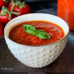 Una ciotola di salsa di pomodoro fatta in casa, guarnita con basilico fresco, con pomodori maturi sullo sfondo.