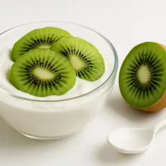 Yogurt con kiwi, un'ottima scelta tra gli alimenti che assorbono i gas intestinali. Una fetta di kiwi accanto a una ciotola di yogurt bianco con tre fette di kiwi sopra.