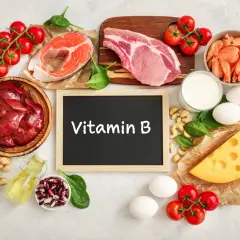Tafel mit "Vitamin B" umgeben von Lebensmitteln wie Fisch, Fleisch, Eiern, Käse, Nüssen und Gemüse.