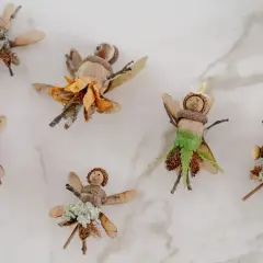 Figuras de hadas hechas con bellotas, ramas y hojas sobre fondo blanco.