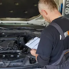 Mechanik sprawdza dokumentację przy otwartej masce samochodu. Czy wymiana oleju poza ASO a gwarancja to dobry pomysł?