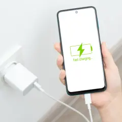 Dłoń trzyma smartfon z ikoną szybkiego ładowania. Obok w gniazdku wtyczka ładowarki. Oszczędzanie baterii nigdy nie było tak proste.