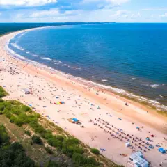 Słoneczne plaże nad morzem tętnią życiem. Tłumy plażowiczów odpoczywają na piasku, kąpią się w morzu i cieszą się wakacjami.