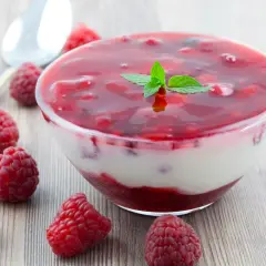 Pyszny deser z galaretki i jogurtu z malinami, udekorowany listkiem mięty. Idealny na letnie popołudnie.
