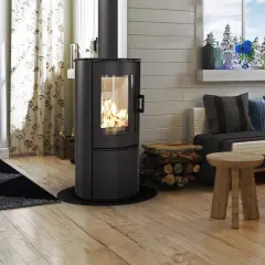Gemütliches Wohnzimmer mit brennendem Kaminofen (BimschV Stufe 2 Liste), Holzstapel, Sofa mit Kissen und Holztisch.