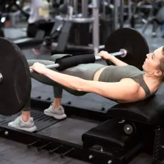 Kobieta wykonuje hip thrust z obciążeniem na ławce. Ćwiczenie to świetnie wzmacnia pośladki i jest możliwe do wykonania nawet w domu.