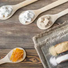 Drewniane łyżki z różnymi rodzajami cukru: kostki, brązowy cukier, karmel i kryształki.